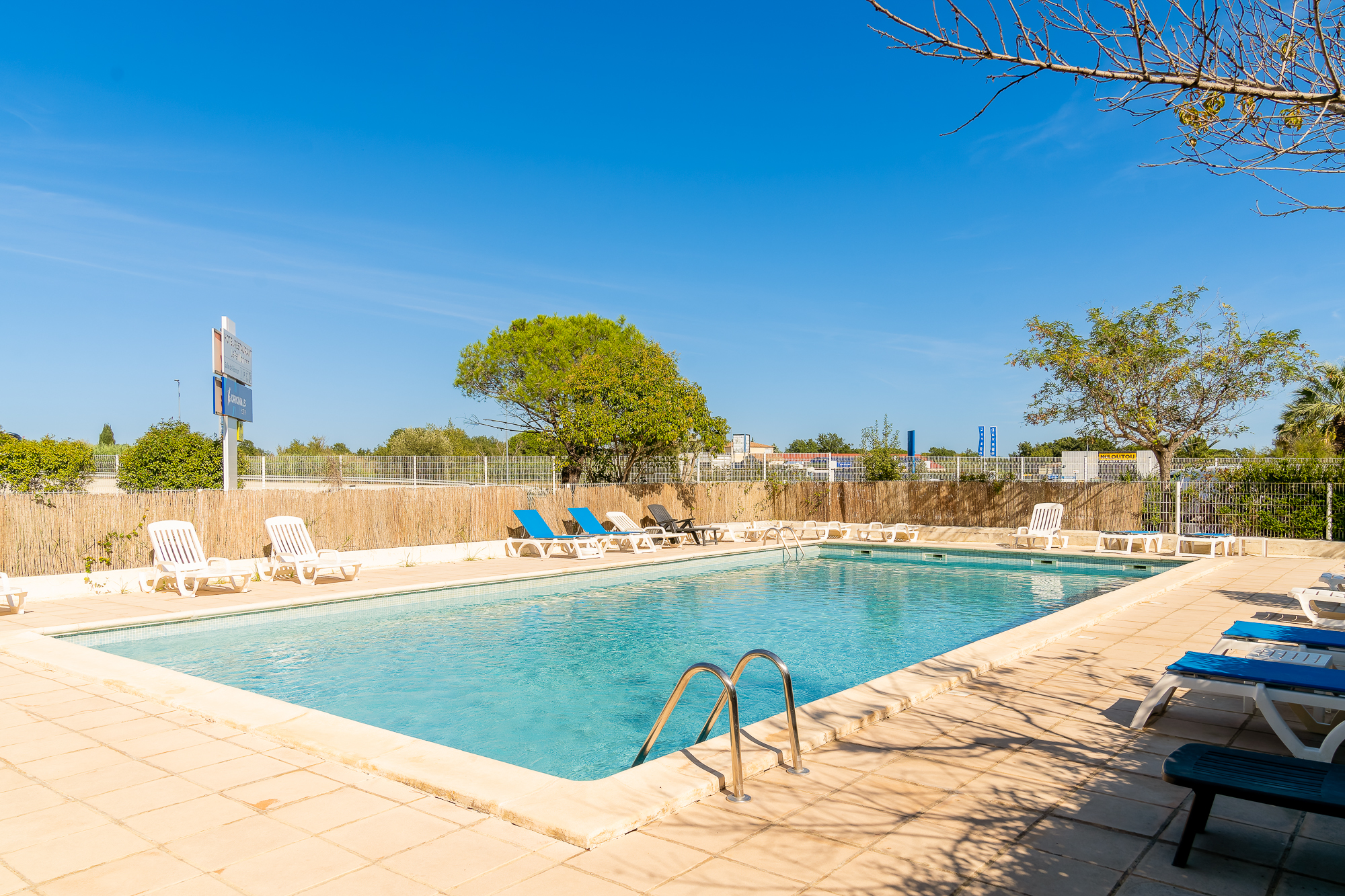 Piscine extérieure entourée de chaises longues sous un ciel bleu sans nuage.