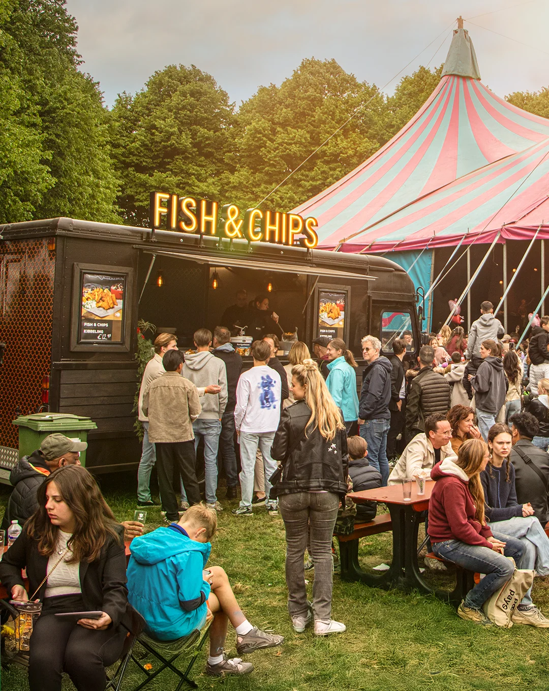 Een foto van een foodtruck met de tekst Fish & Chips, de foodtruck staat op een festival naast een festival tent.