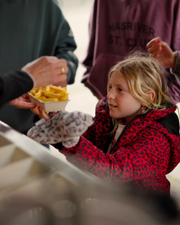 Een meisje krijgt een bakje friet aangerijkt.