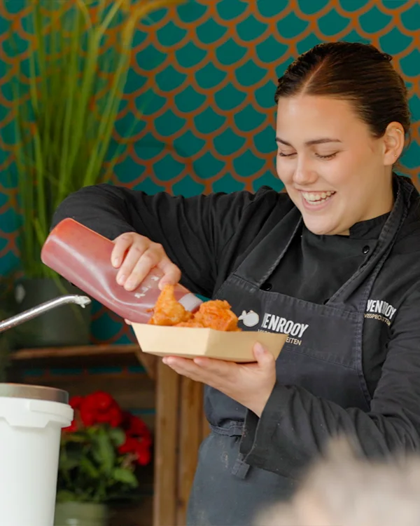 Een vrouw die saus bij een bakje kibbelingen serveert.