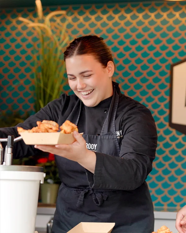 Een vrouw die saus bij een bakje kibbeling schept.