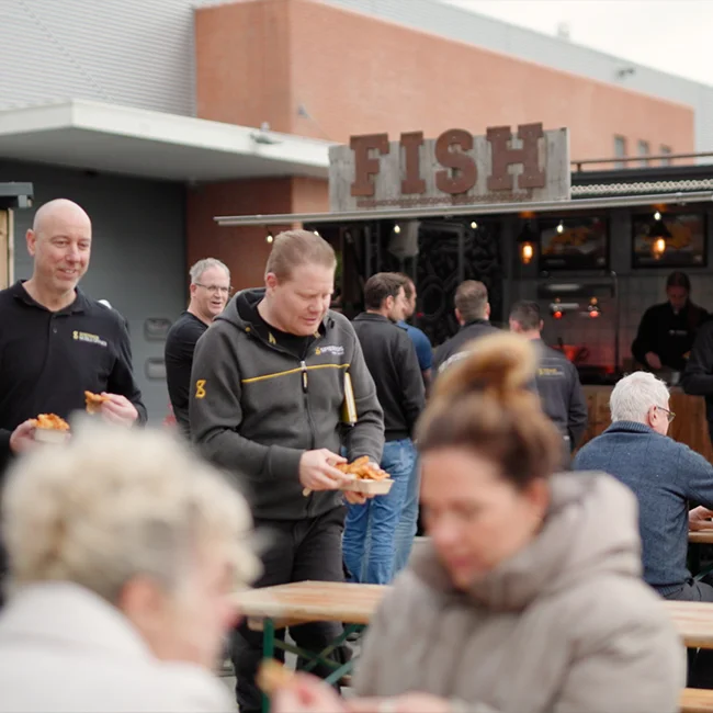Een aantal mensen die voor een foodtruck staan met daarop FISH.