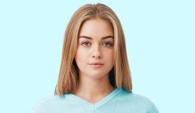 Portrait of a young woman with straight blonde hair wearing a light blue sweater on a pale blue background.