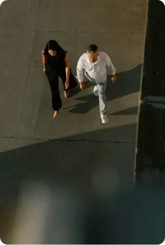 Overhead view of a man in white and a woman in black walking side by side on a pavement.