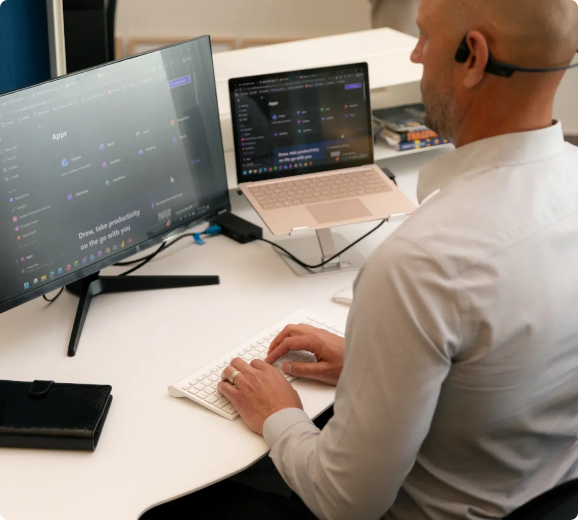 Man in white shirt using wireless keyboard with dual monitors showing productivity app screens.
