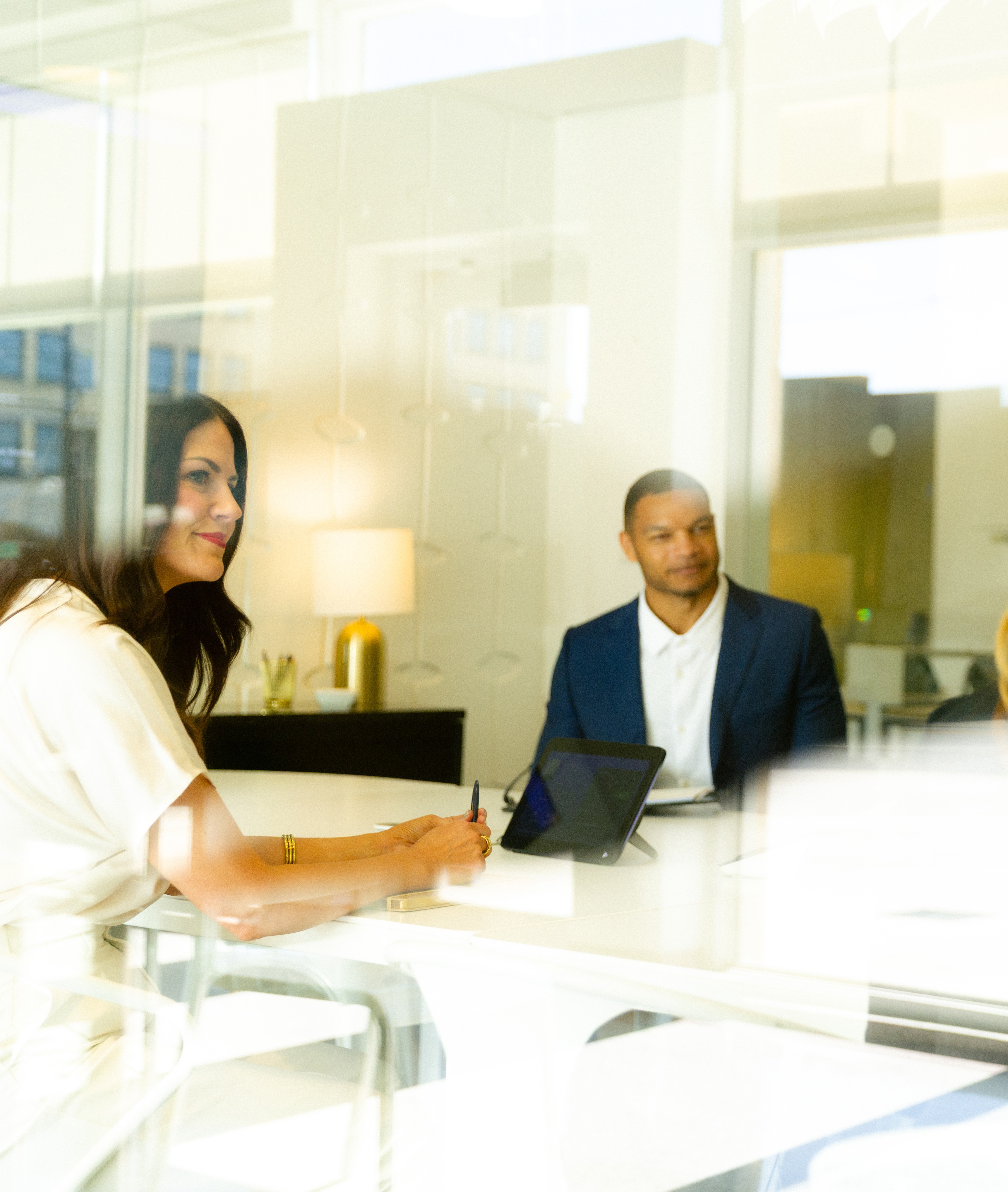 Two business professionals sitting at a table in a modern office meeting room with a tablet.