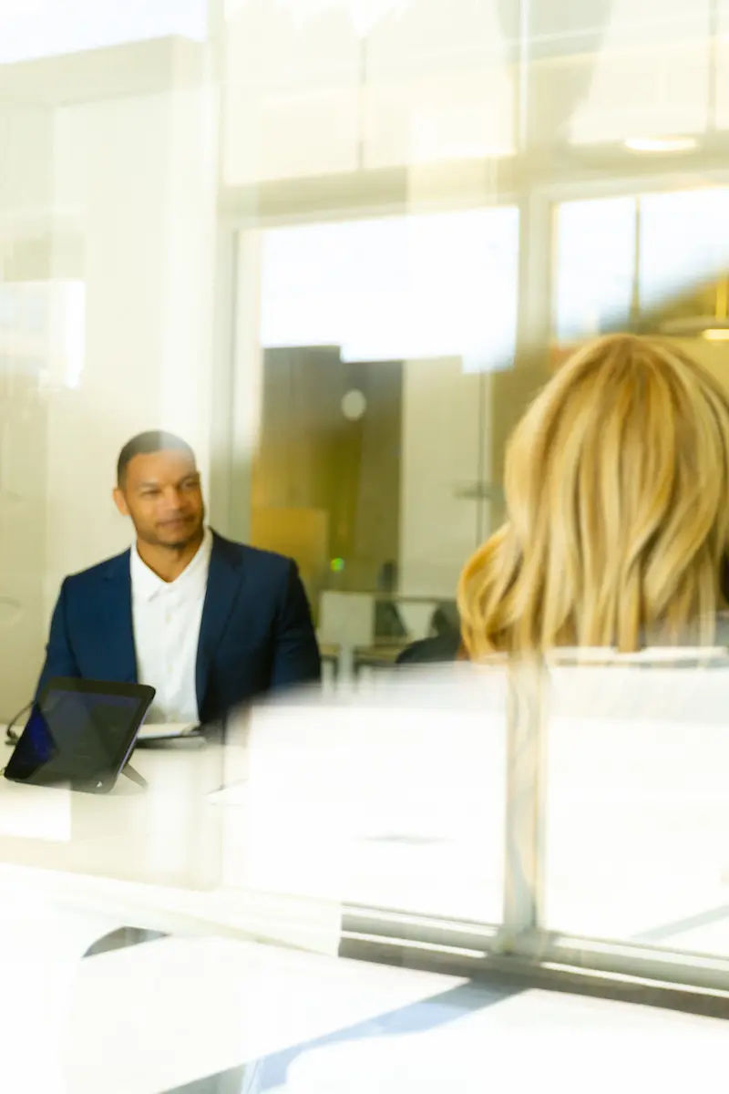 Man in a suit and a woman with blonde hair having a meeting in a bright office with glass walls.