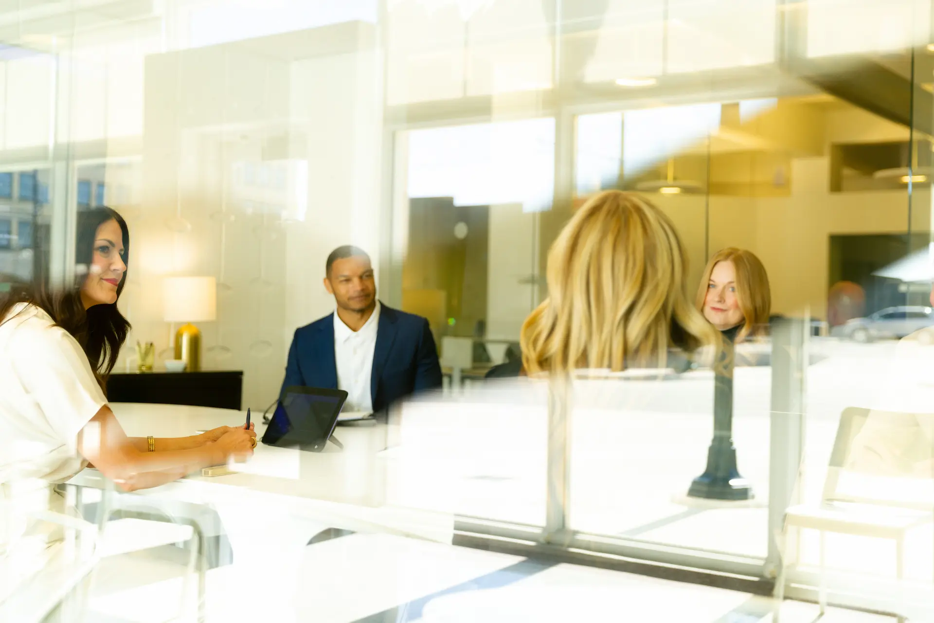 Four professionals in a modern office glass conference room engaged in discussion around a white table.