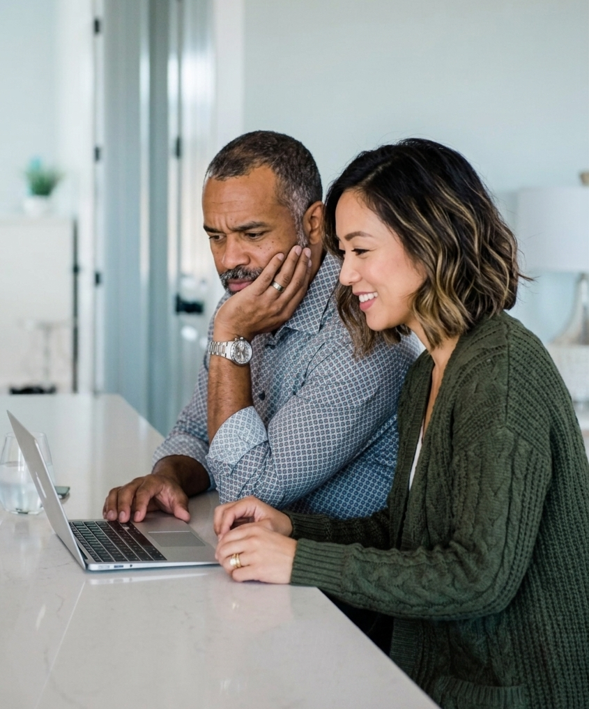 Un homme et une femme souriante regardent un ordinateur portable ensemble dans un bureau à domicile.