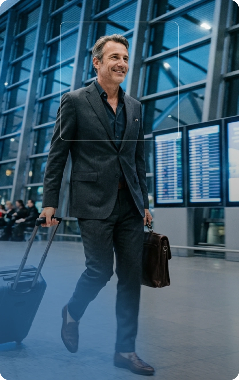 Homme d'affaires souriant en costume marchant dans un aéroport avec une valise et une mallette.
