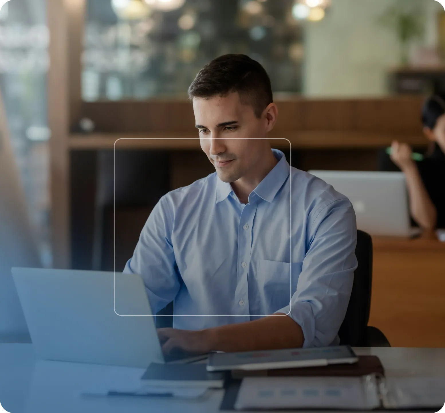 Jeune homme en chemise bleue travaillant sur un ordinateur portable dans un bureau moderne.