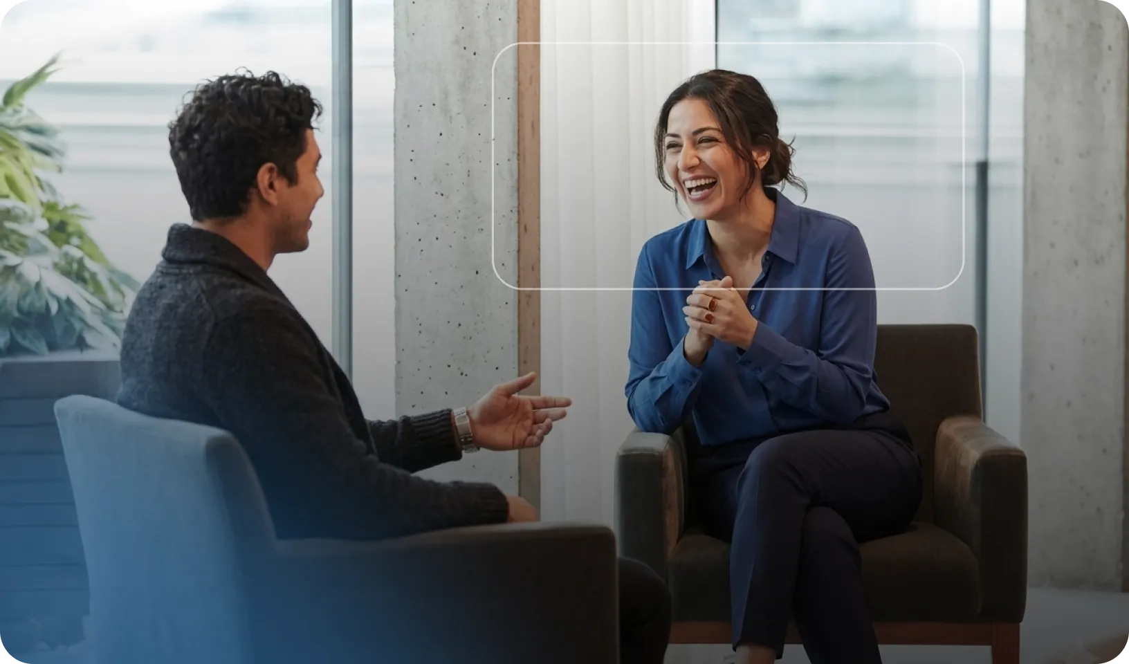 Un homme et une femme sont assis en face à face, discutant et souriant dans un bureau moderne.