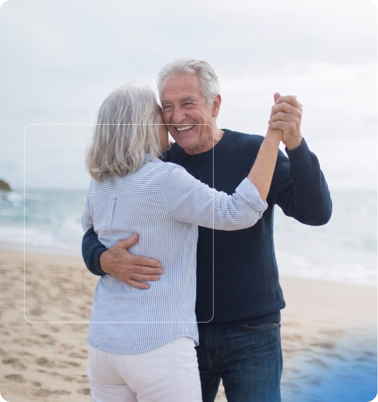 Un couple âgé danse et rit sur une plage au bord de la mer.