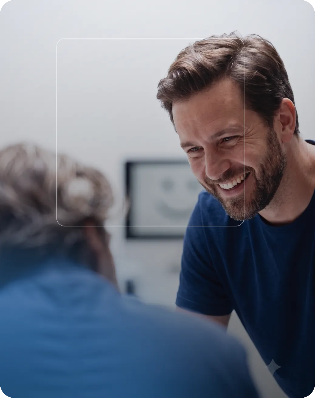Un homme souriant regardant son reflet dans un miroir, portant un t-shirt bleu.