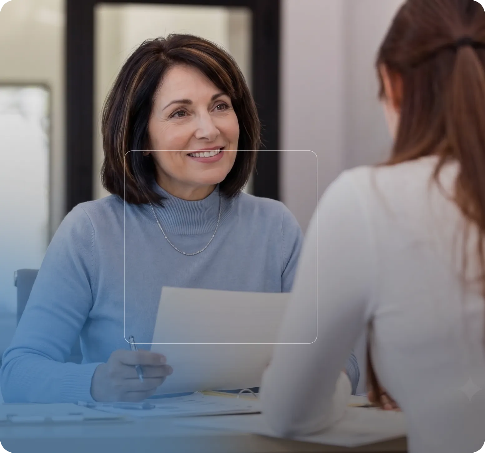 Une femme souriante tenant un document en conversation avec une autre personne vue de dos.