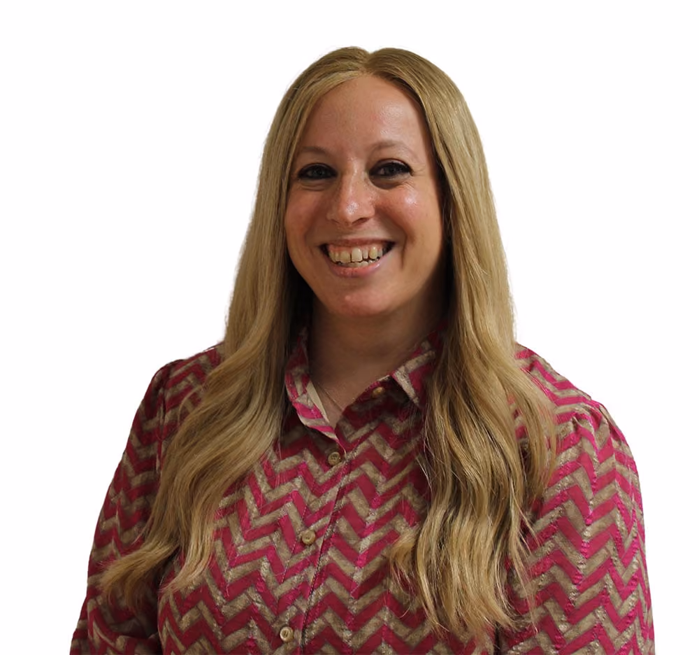 Smiling woman with long blonde hair wearing a pink and beige zigzag patterned shirt.