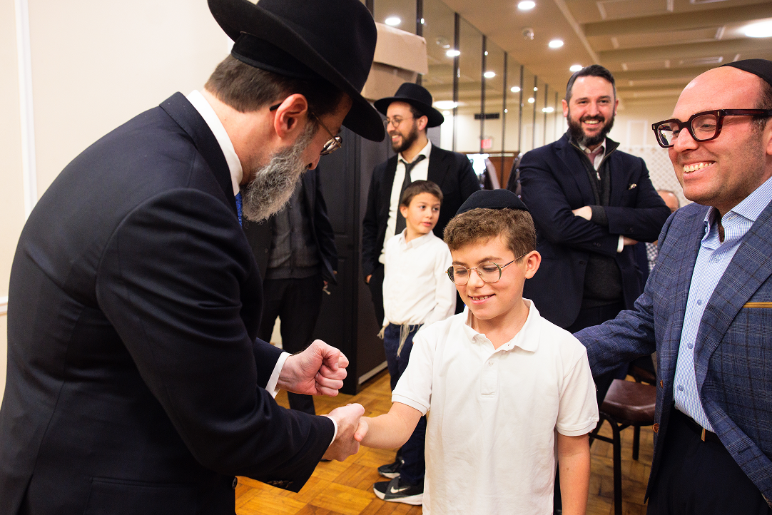 A boy in white shirt shakes hands with a man in black hat and suit while others watch and smile.