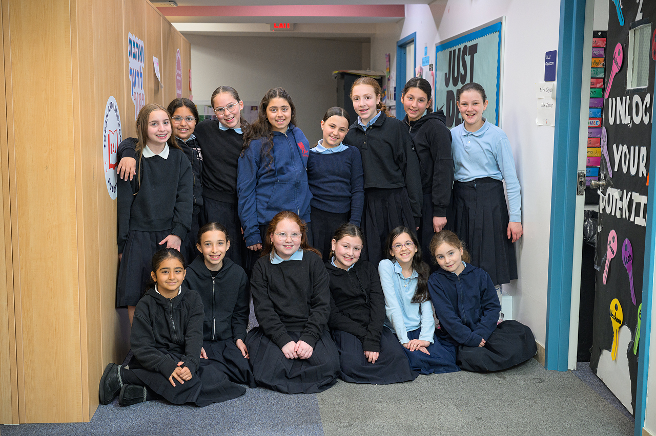 Group of smiling girls in school uniforms posing in a hallway with motivational signs on walls.