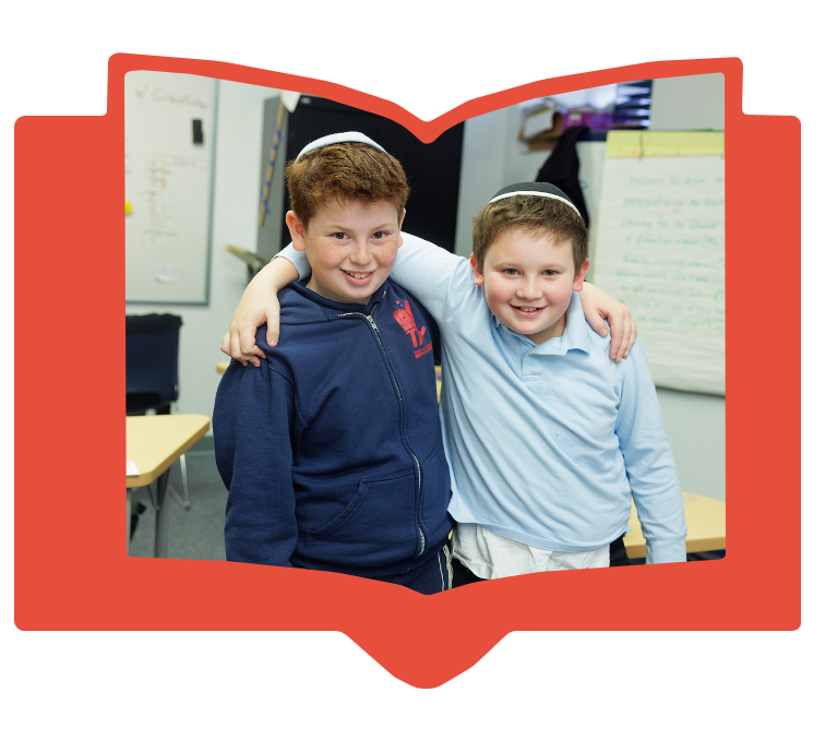 Two boys wearing kippahs with arms around each other smiling in a classroom framed by a red book shape.