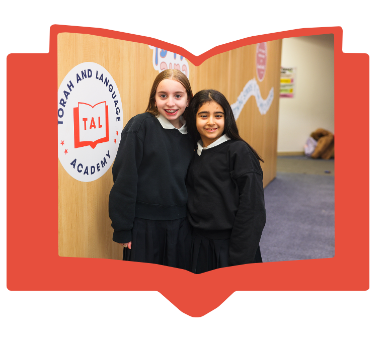 Two smiling schoolgirls in black uniforms standing inside Torah and Language Academy.