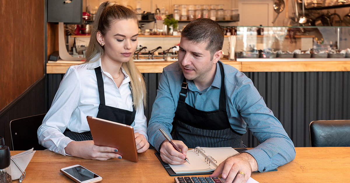 Two small business owners reviewing figures with a calculator and notebook