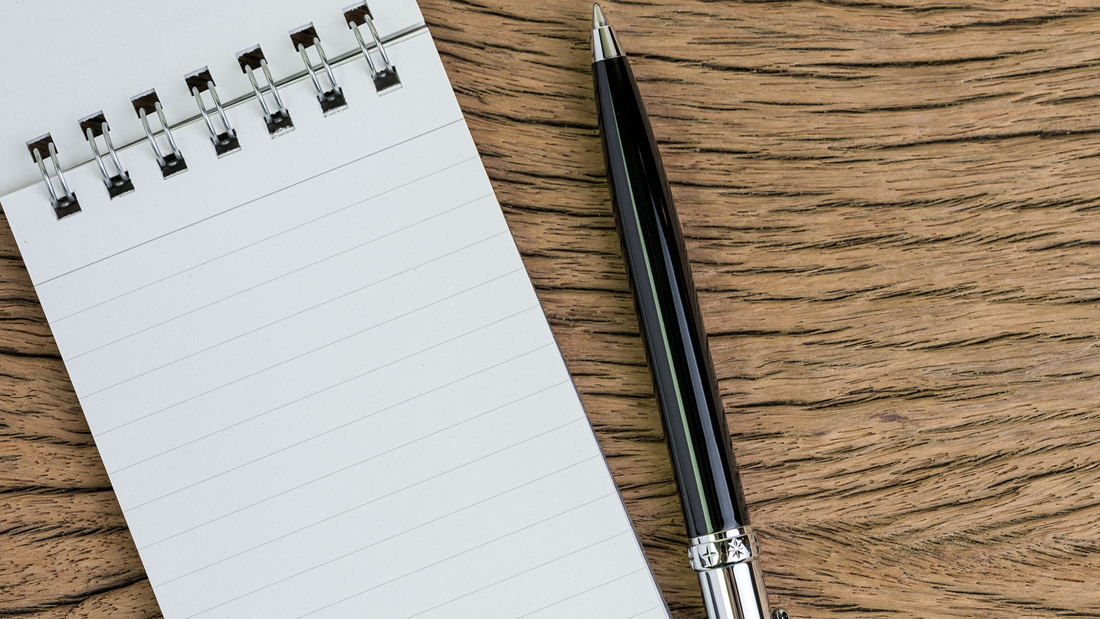Notepad and pen on a wooden desk ready for a list of questions