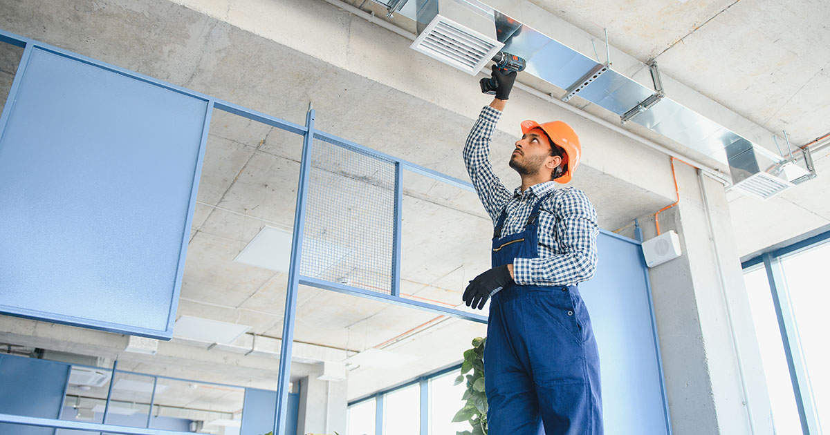 HVAC technician installing overhead ductwork and a ceiling air vent on a Tampa service call