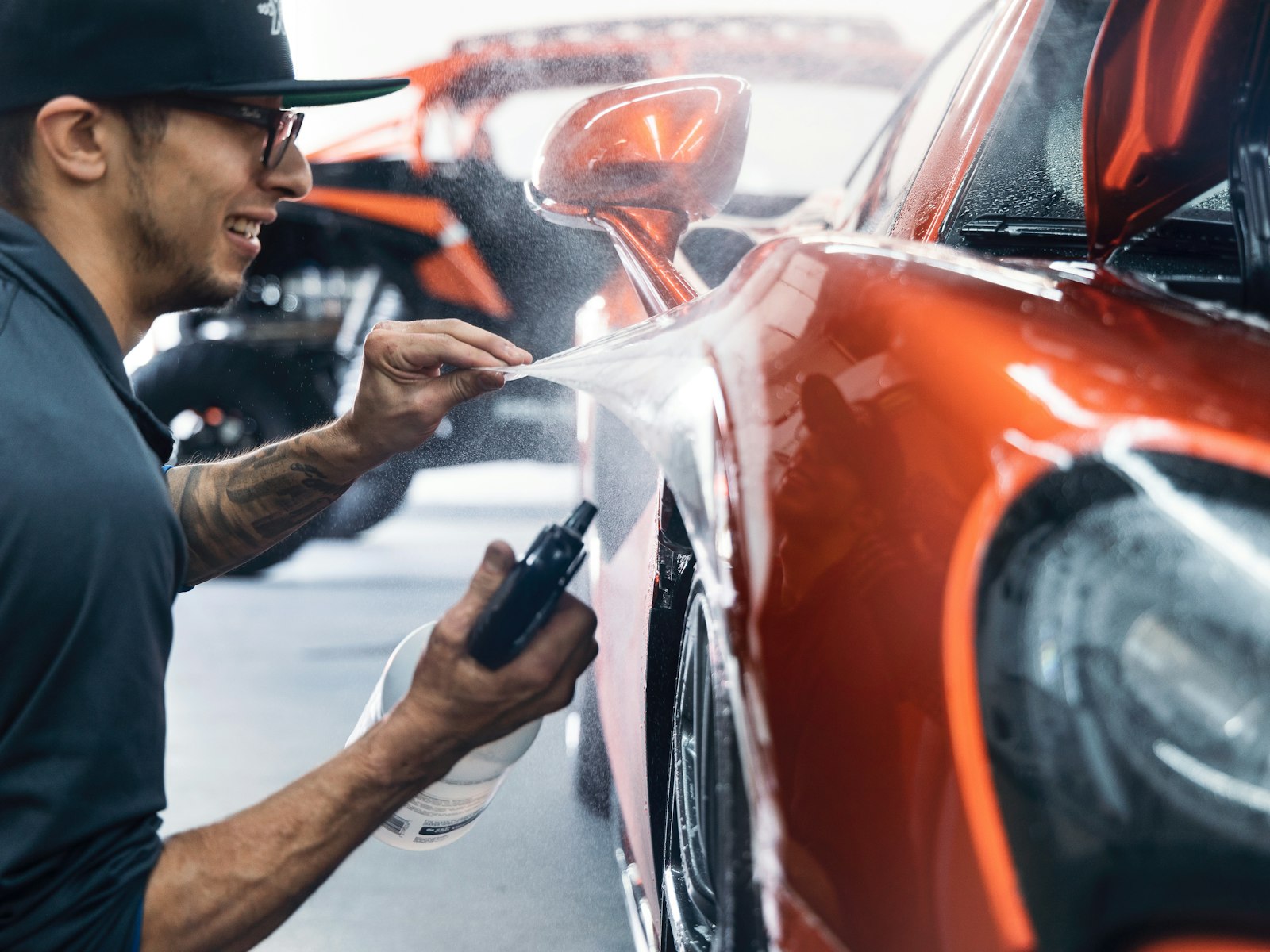 Technician finishing the body panel of an orange sports car