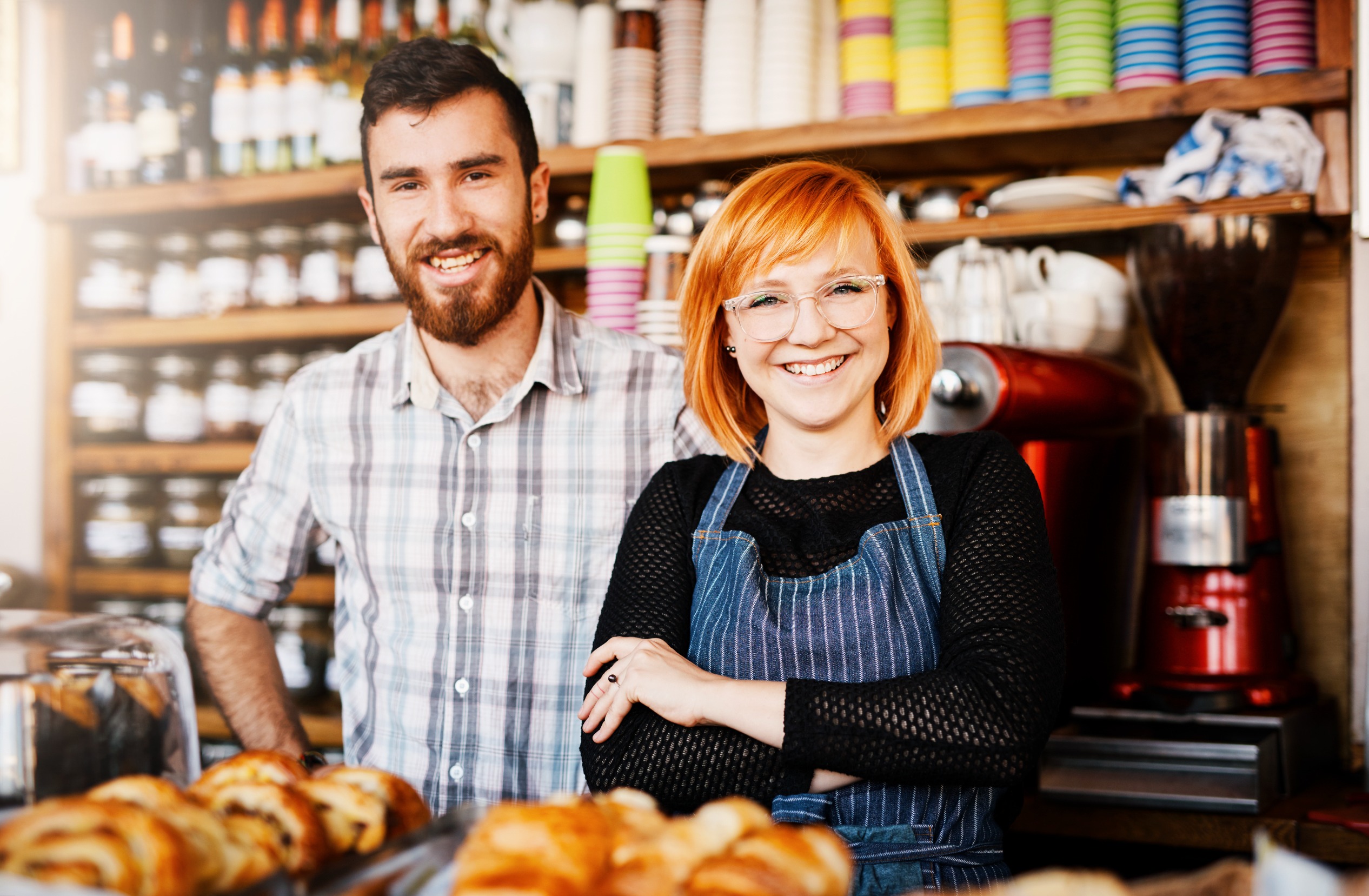 Two smiling cafe owners behind the pastry counter of their shop
