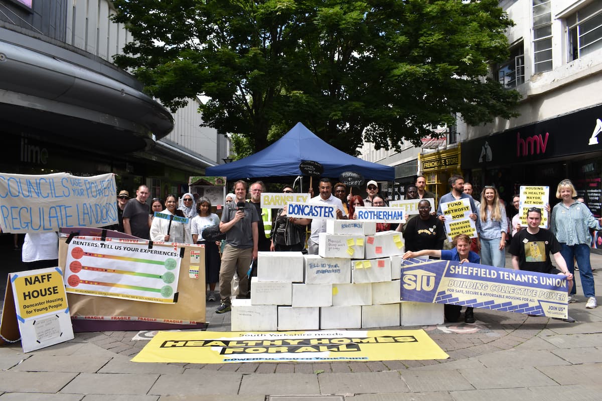 Dozens of Powerful South Yorkshire members at the 'Homes for People, not Profit' event in Doncaster. There is a large tree behind them, various banners 'Councils use your power, regulate landlords.' 'South Yorkshire residents want Healthy Homes for All.' 'Fund retrofit now.' and more.