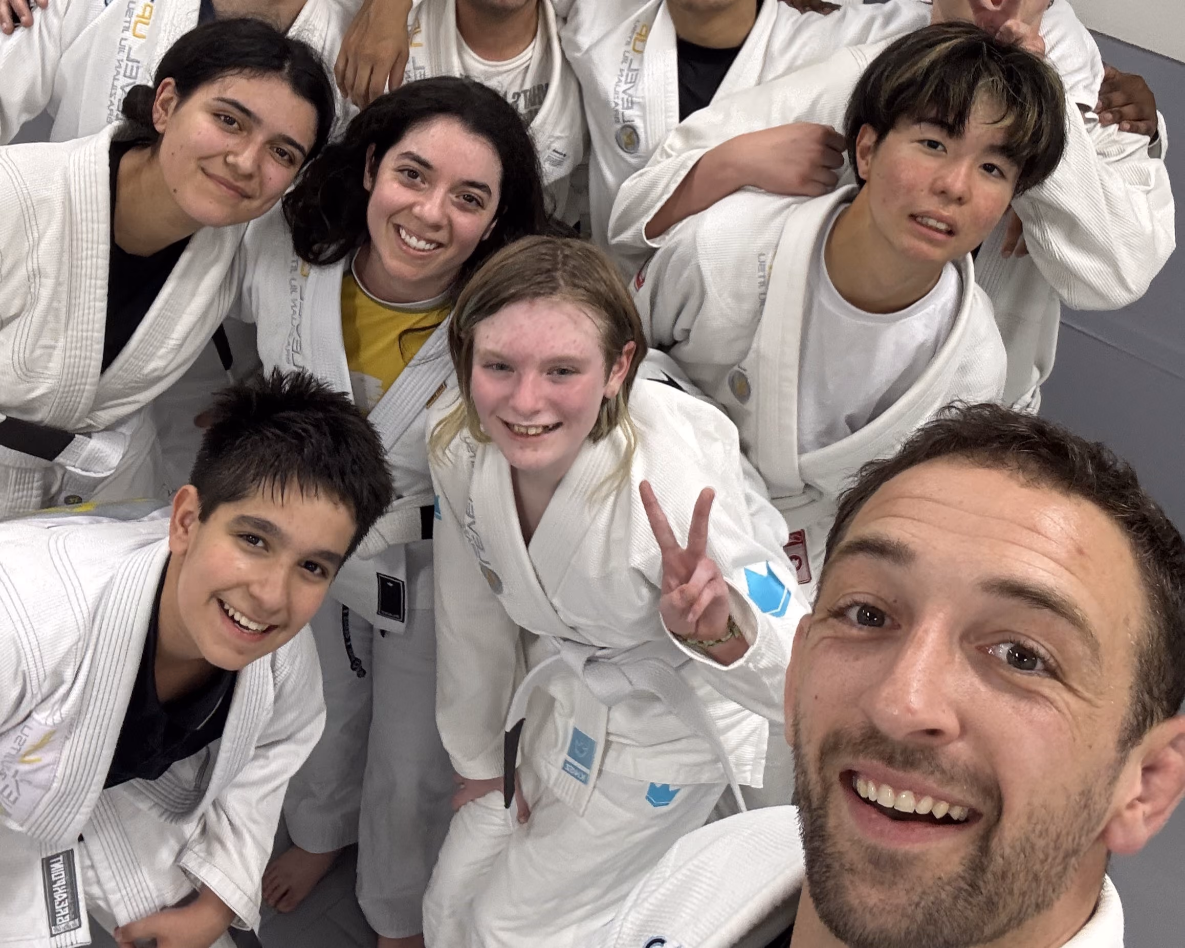 Smiling group of young judo practitioners posing for a selfie in white gis on a mat.