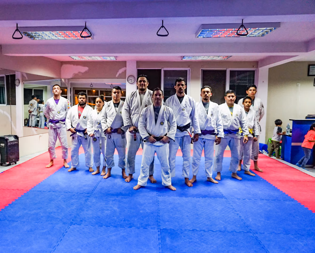 A group of people in white martial arts uniforms standing on blue and red mats in a dojo.