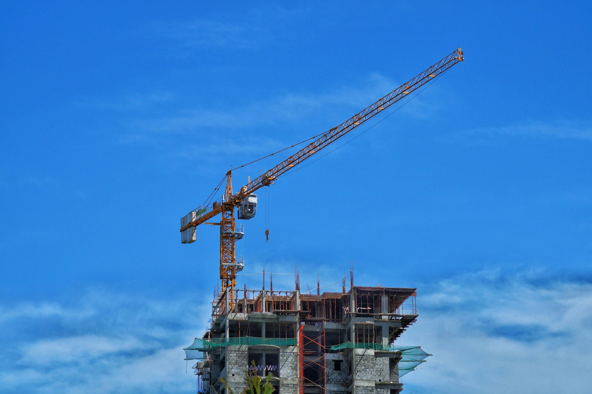 Construction crane towering over a multi-story building under construction against a clear blue sky.