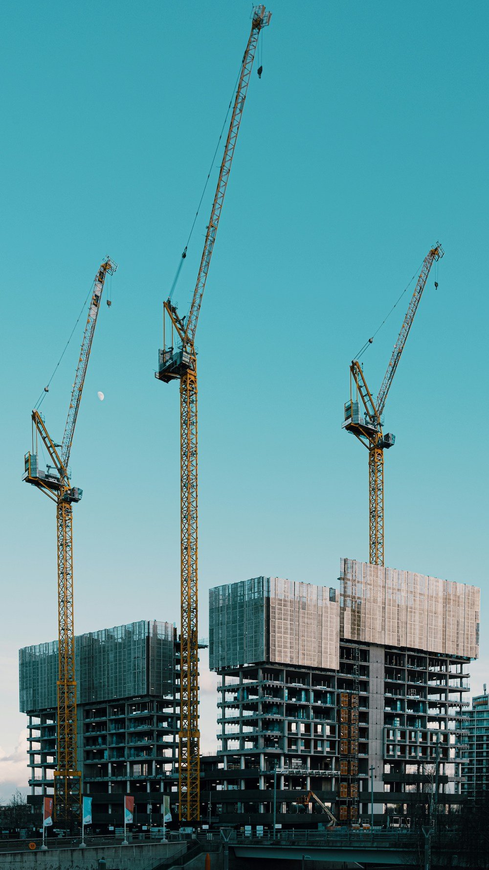 Three tall construction cranes working on two high-rise buildings under construction.
