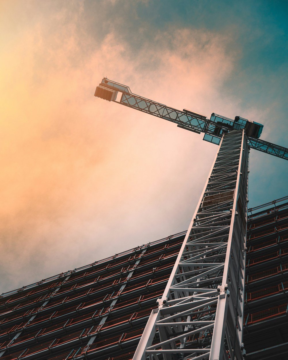 Low-angle view of a construction crane next to a building under a dramatic sunset sky.