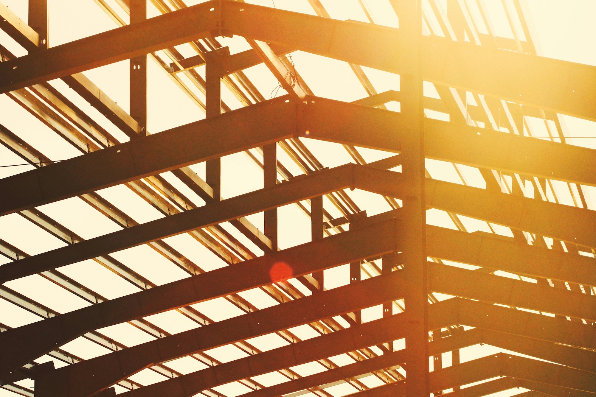 Sunlight shines through the metal framework of a building under construction.