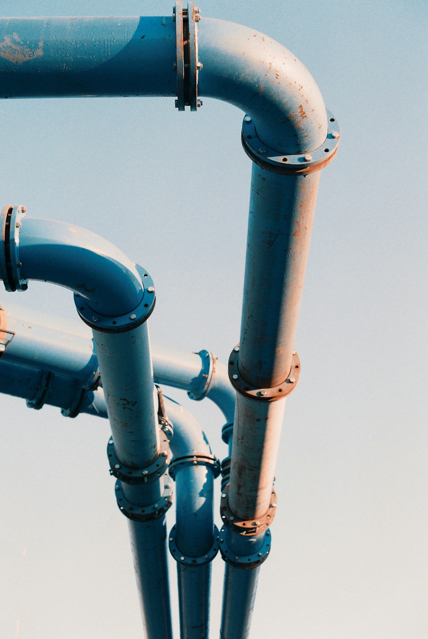 Close-up of large blue industrial pipes with flanged joints against a clear sky.