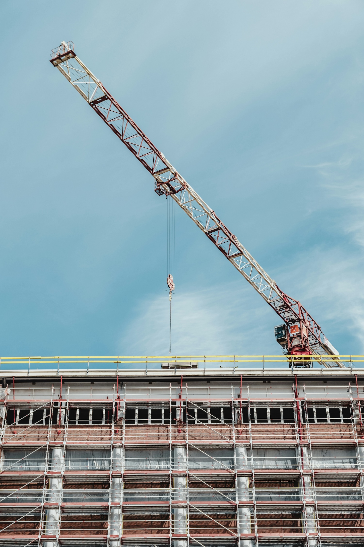 Tower crane above a building under construction with scaffolding and a clear blue sky background.