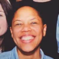 Personne très souriante avec des cheveux courts et qui porte une chemise bleue claire.