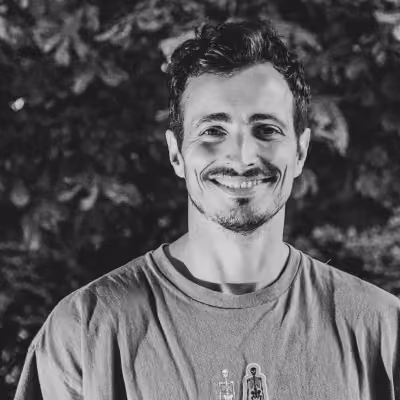 Portrait en noir et blanc d'un homme souriant avec un t-shirt, fond de feuillage flou.
