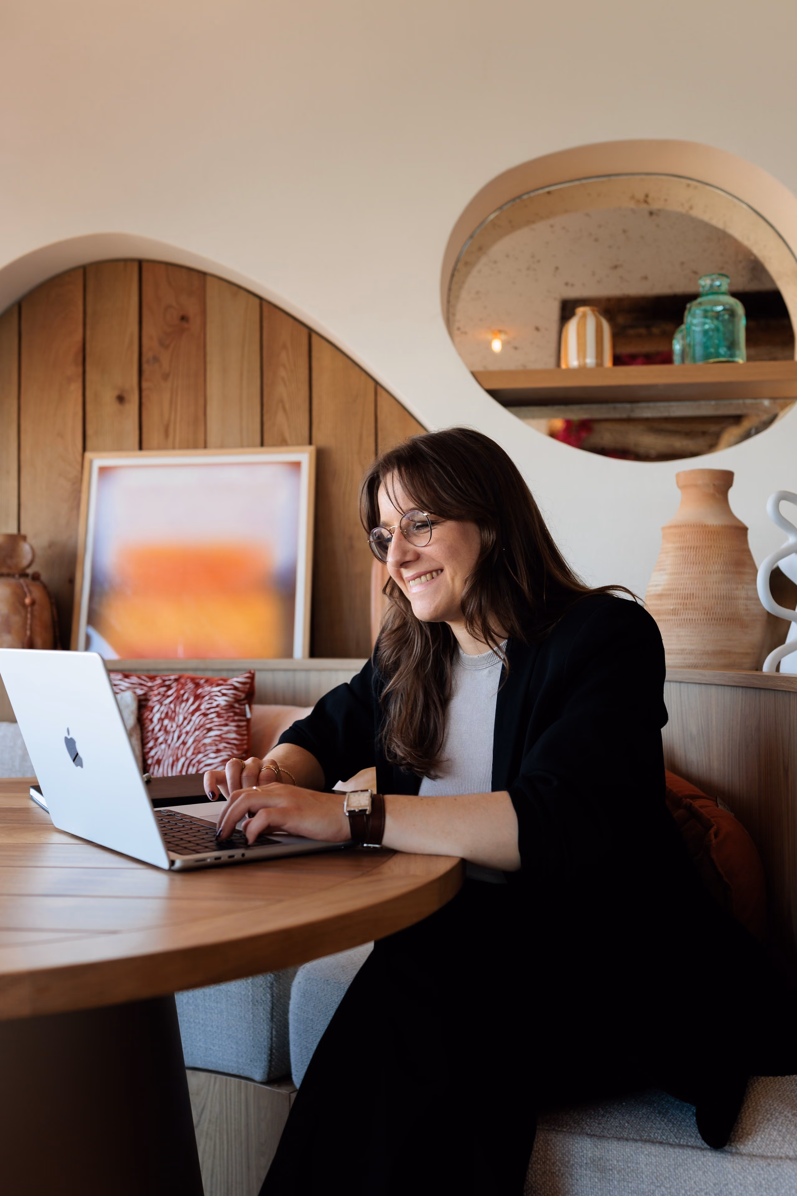 Jeune femme souriante tapant sur un ordinateur portable dans un espace cosy avec décoration murale.