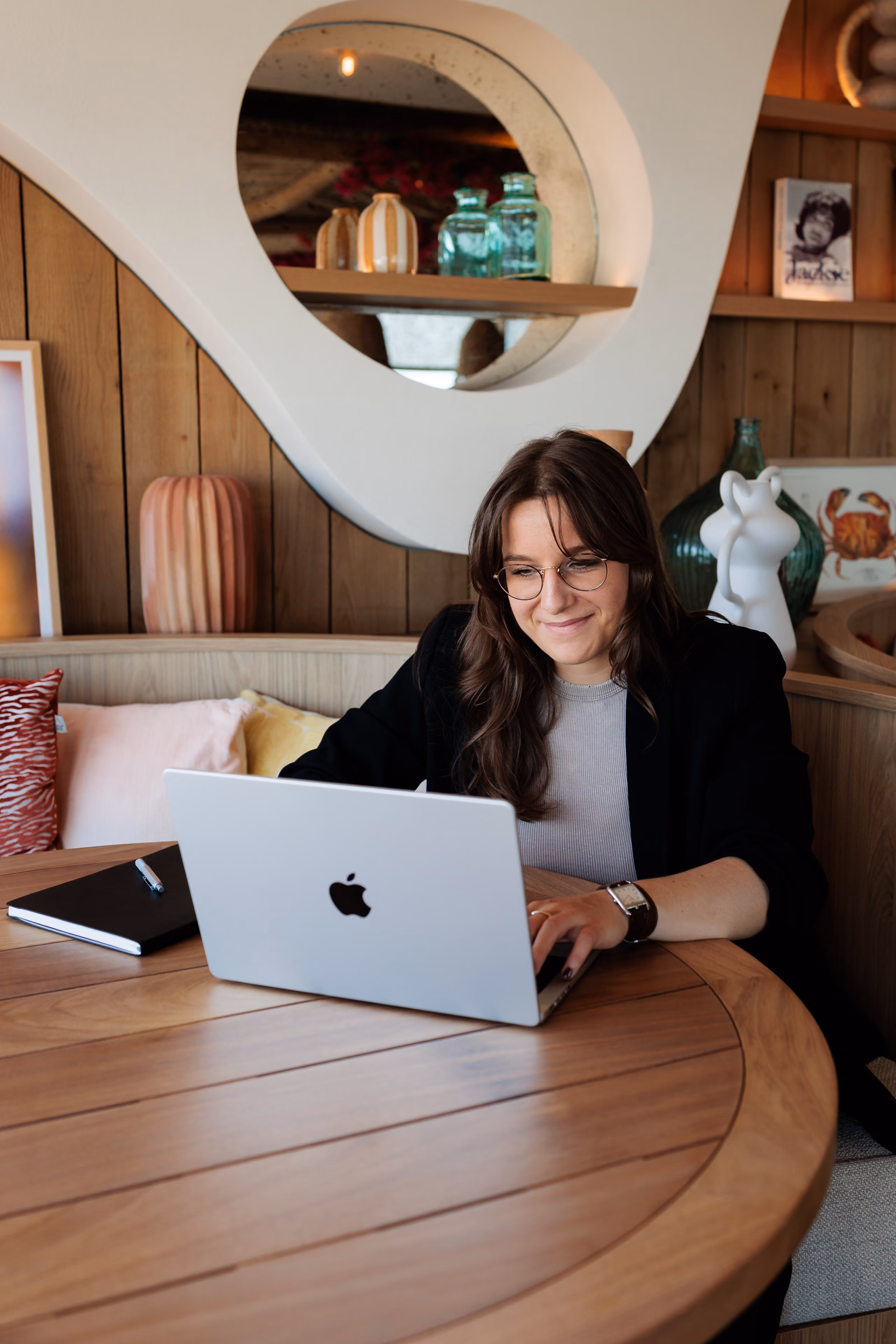 Femme souriante travaillant sur un ordinateur portable Apple à une table en bois rond.