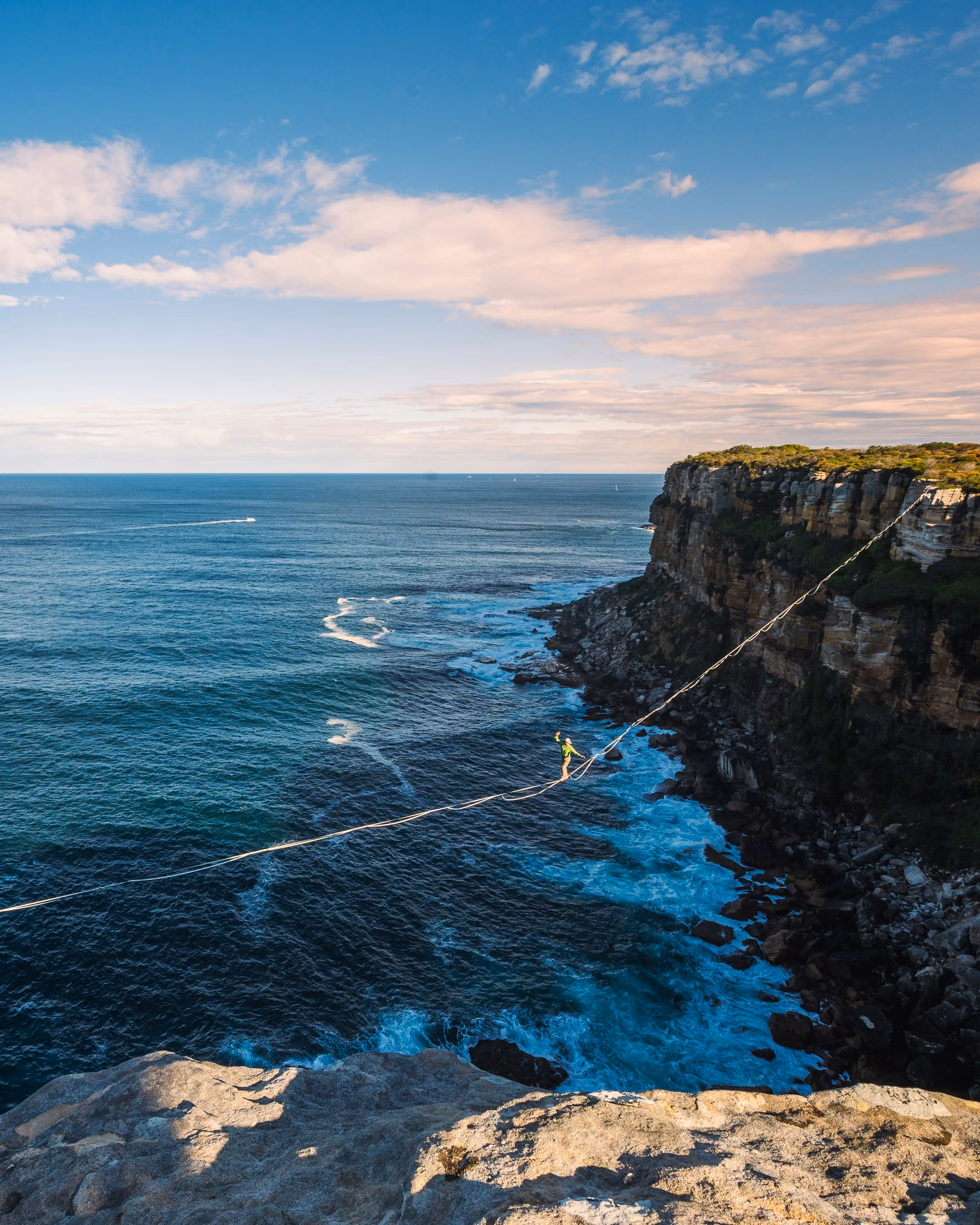 Personne marchant sur une corde tendue au-dessus de la mer entre deux falaises rocheuses.