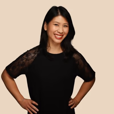 Femme souriante aux cheveux noirs, portant un haut noir avec manches en dentelle, posant les mains sur les hanches.