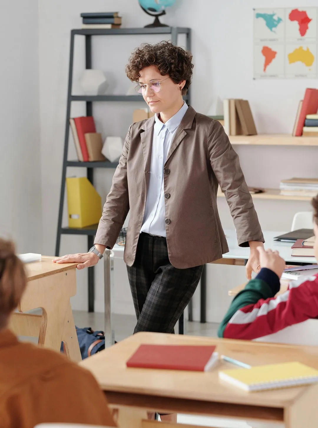 A teacher stands in the middle of the classroom between the desks