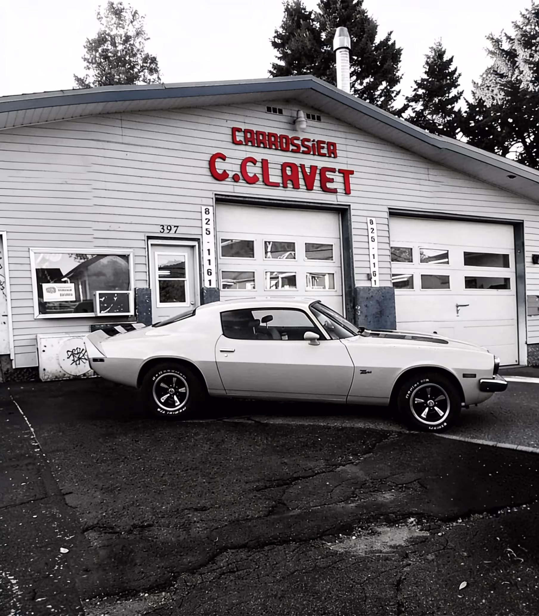 Classic car parked outside a garage with sign reading 'Carrossier C. Clavet' in red letters.