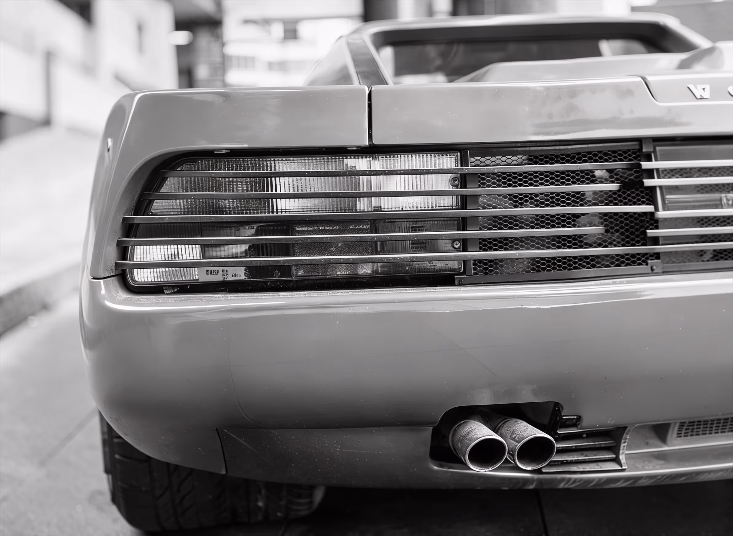 Black and white close-up of a vintage car's rear showing exhaust pipes and tail light grille.