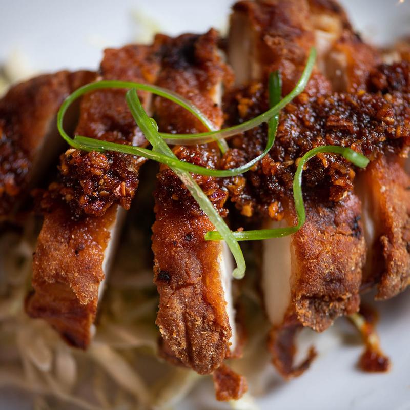 Close-up of crispy fried chicken slices garnished with chopped green onions and spices.