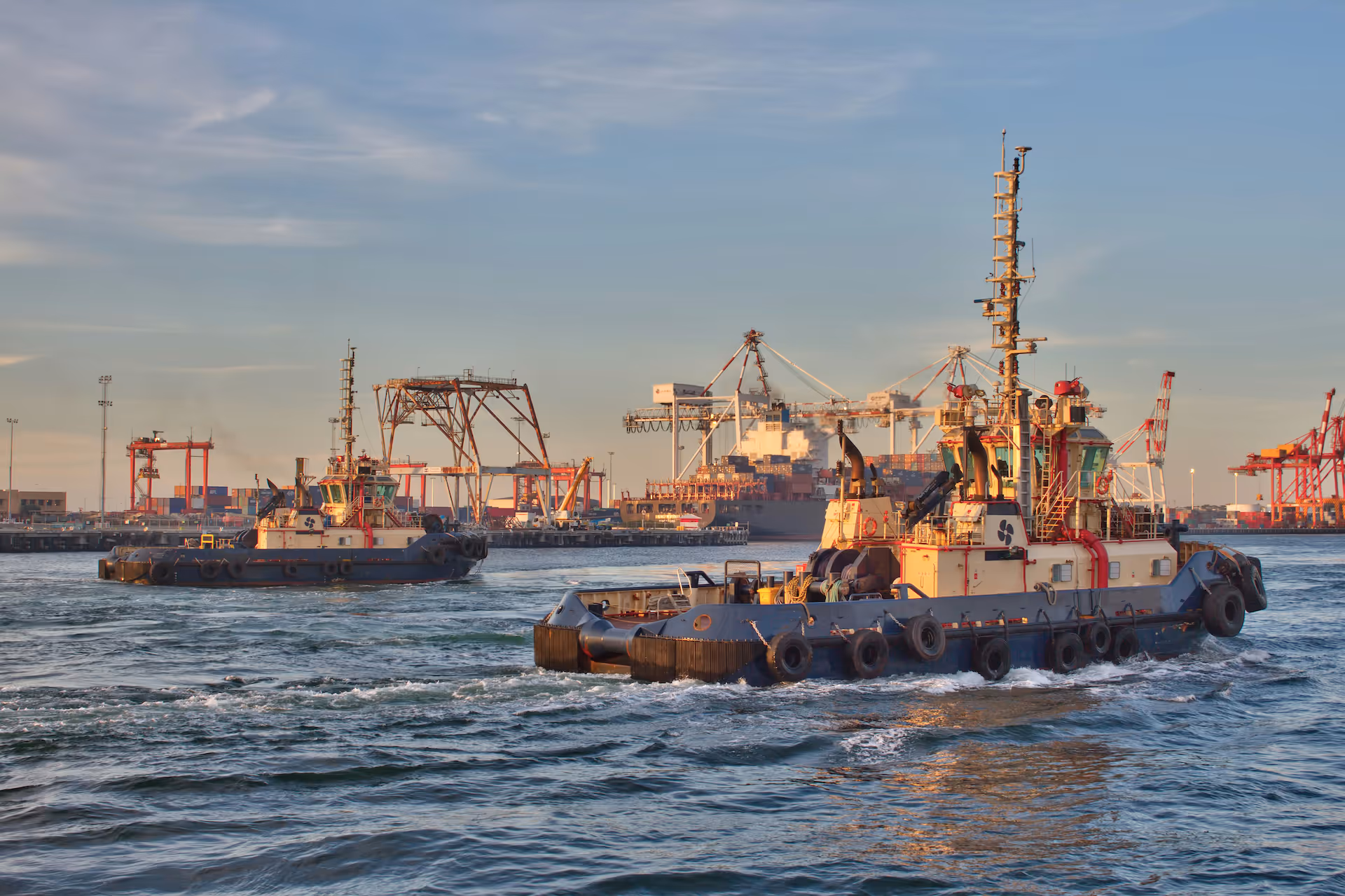 Tugboat working in a busy port with cranes behind