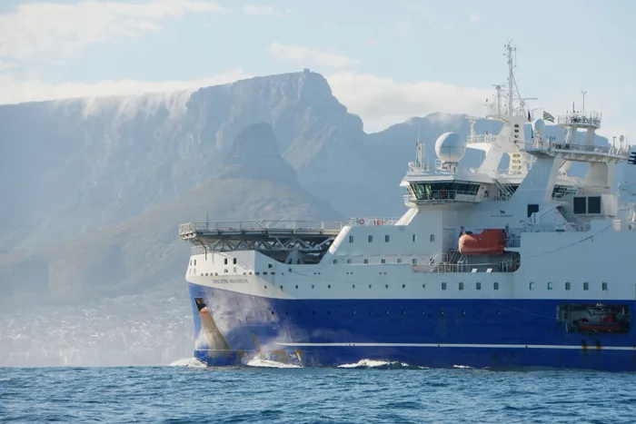 Survey vessel at sea below snow-covered cliffs